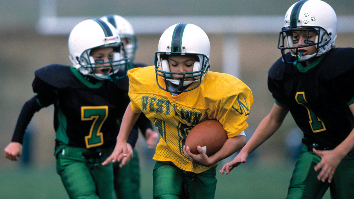 An athlete is running and carrying a football tucked against their body.
