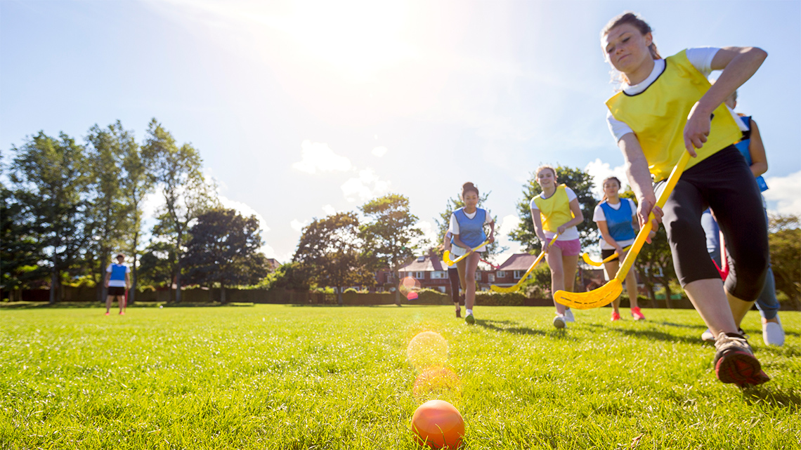 A person holds a field hockey stick as they move with a ball on the field.