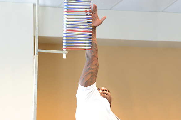An athlete completes a vertical jump test to measure how high he can jump. He jumps with one arm stretched towards the ceiling.