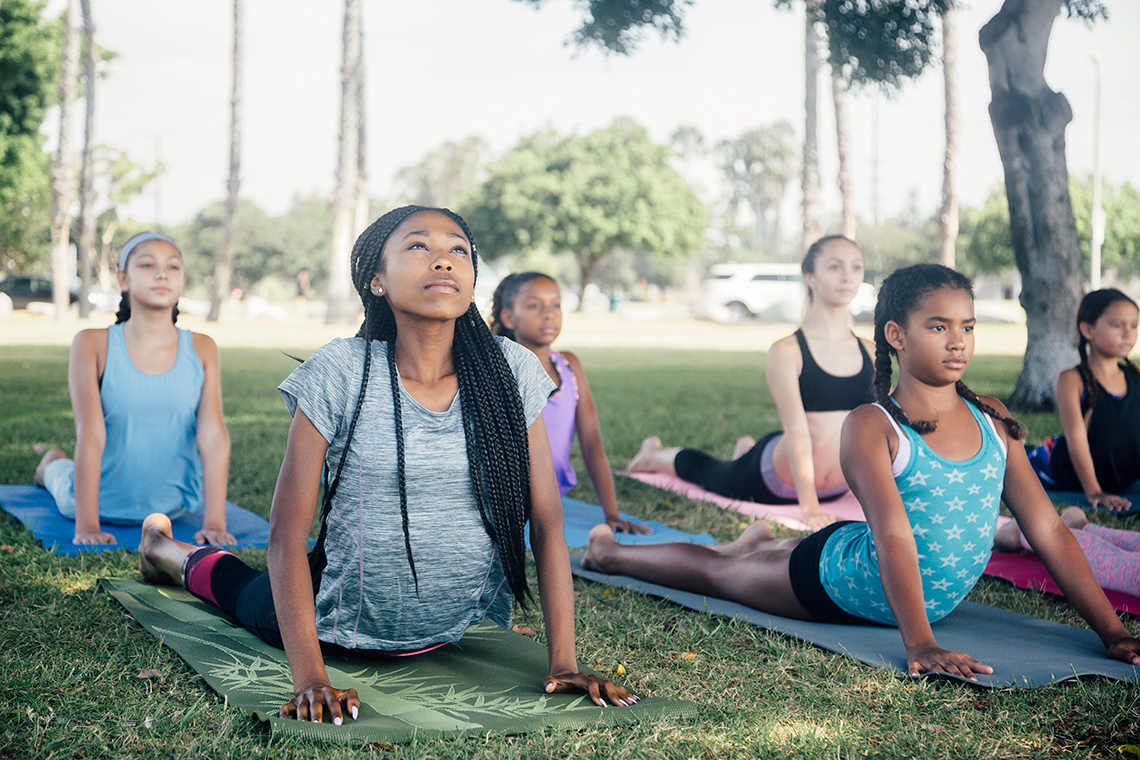 A group of girls doing yoga outside. They lie on mats stretching their backs.