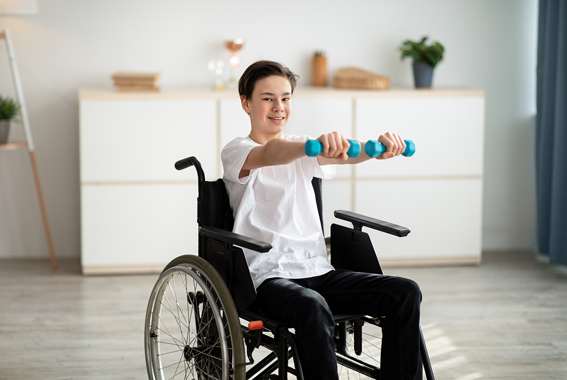 A young person in a wheelchair with arms outstretched and holding dumbbells in each hand.