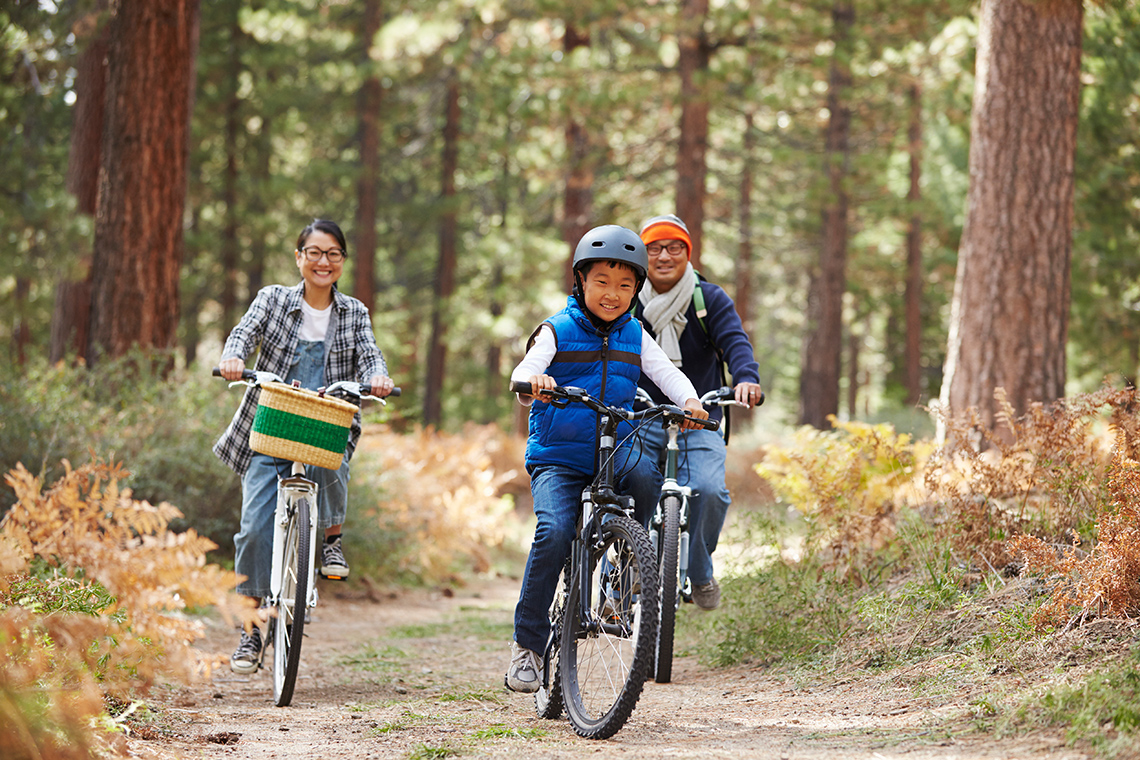 A family of three is biking through a forested path.