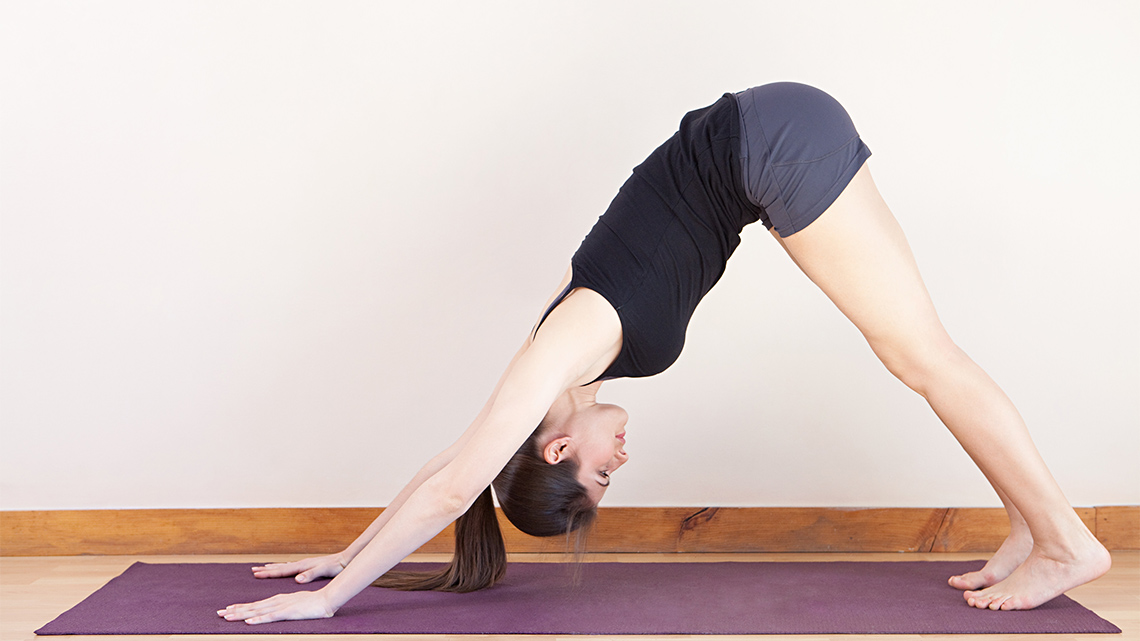 A woman stretching by placing both her hands and feet on the floor and raising her hips to form a triangle with her body.