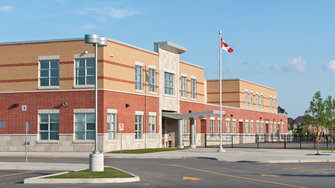 A 2-storey building with a fenced-off playground and a parking lot.