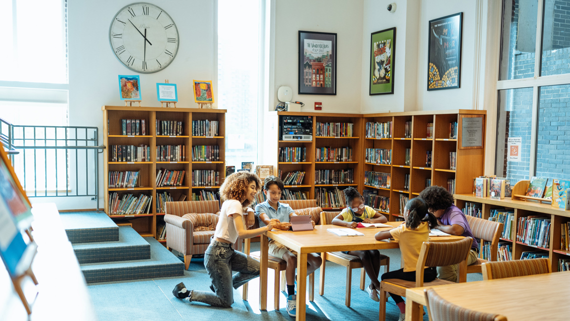 A room full of books on shelves. People are sitting at tables and reading.