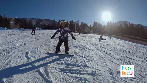 Natalya and Adriana are outside on a hill taking a snowboard lesson.