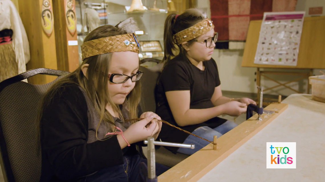 Natalya and Adriana are at a table making cedar bracelets.