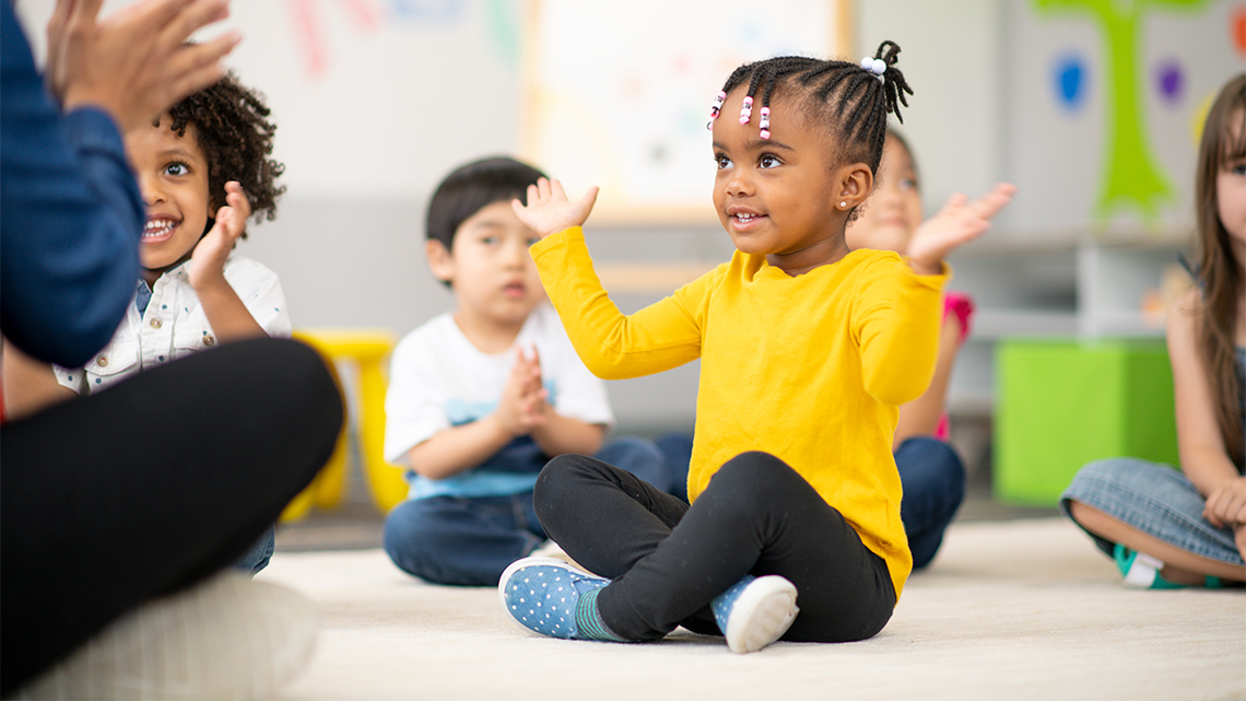 Children clapping hands while sitting in a room with an adult leading them in an interactive song.