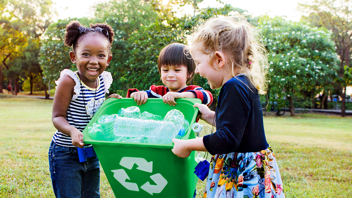 Three children are holding a recycling bin filled with plastic bottles.