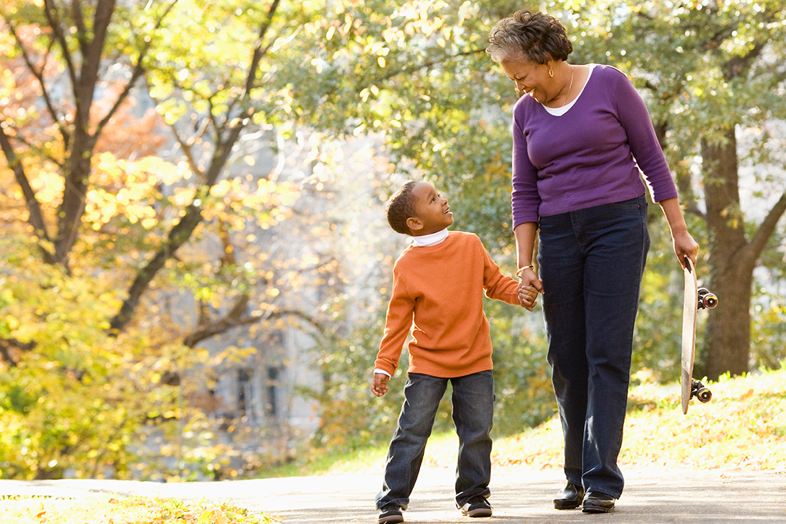 A child is walking through a park space on a path with an adult.