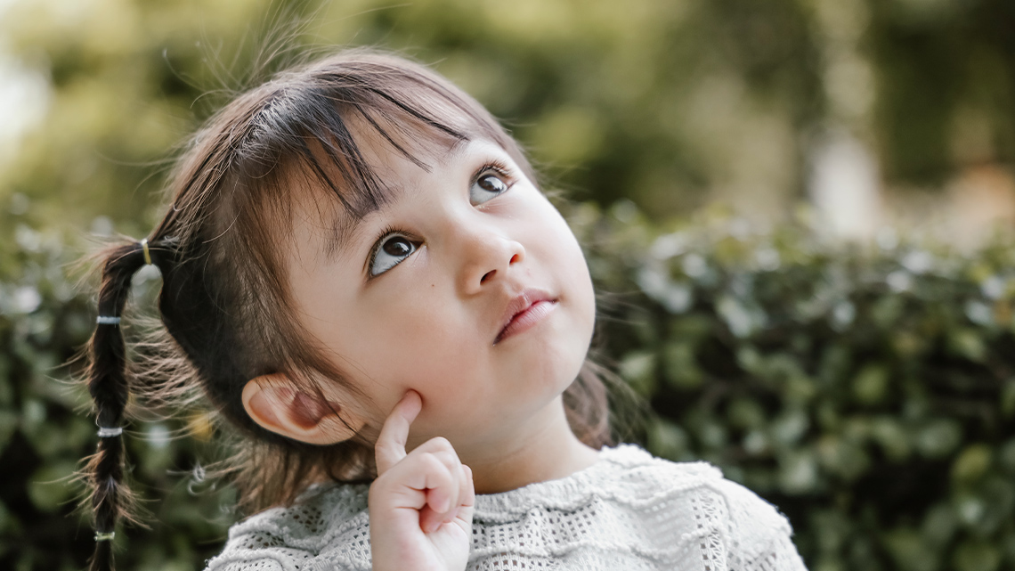 A child looks up and touches their cheek with one finger.