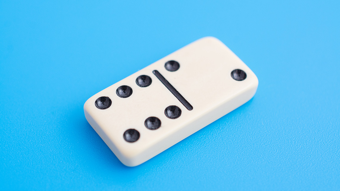 A domino lies on a surface. One half of the domino shows six dots, and the other half shows two dots.
