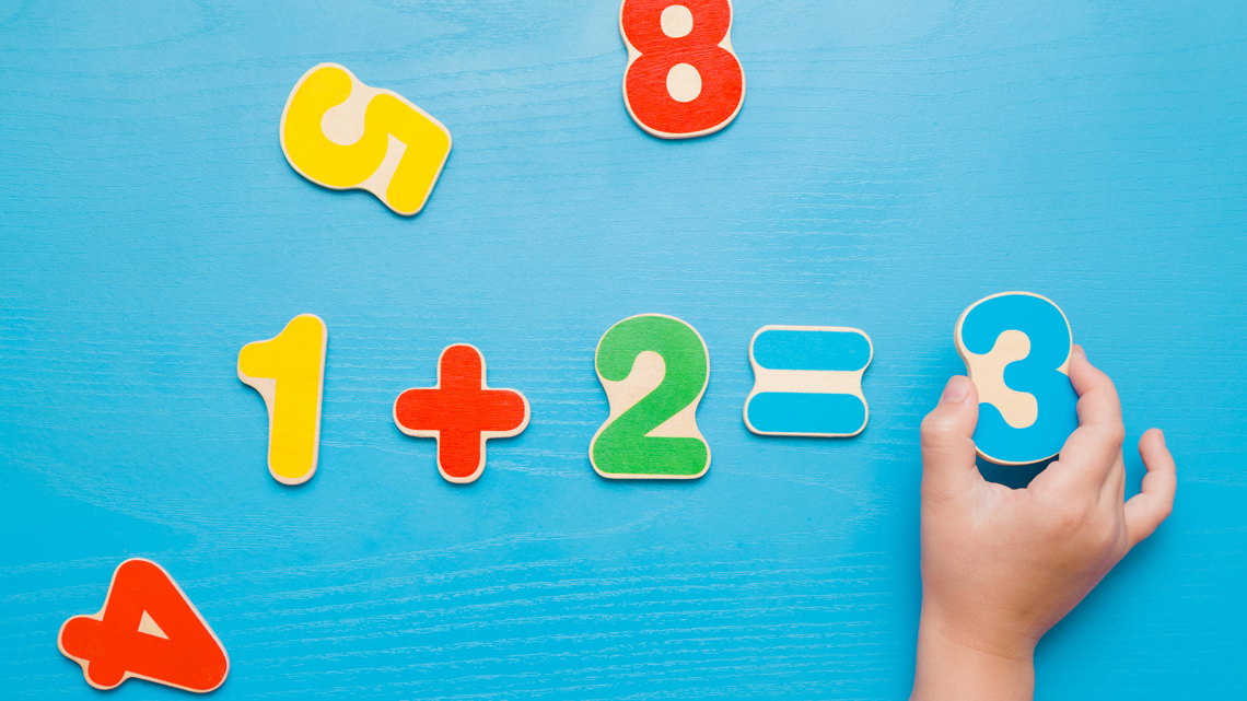 Number pieces are arranged on a surface to form the number sentence '1 + 2 = 3.'