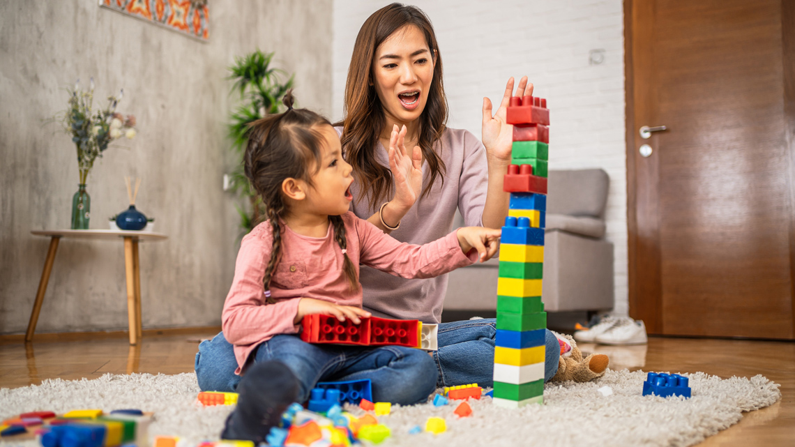 An adult and a child are building a tower with blocks on the floor.
