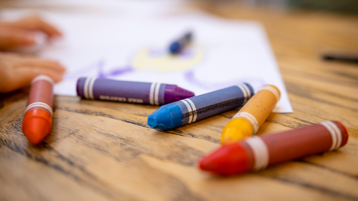 Paper and crayons are on the table. The crayons are scattered everywhere.