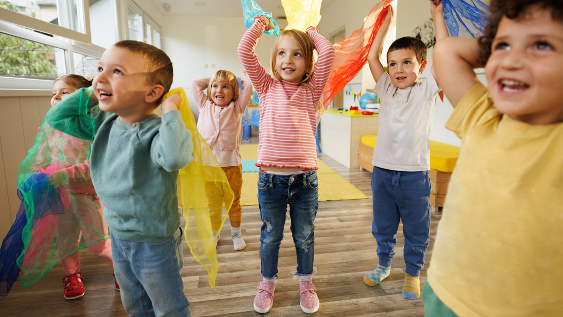 Six kindergarten-aged children are dancing on a carpet.