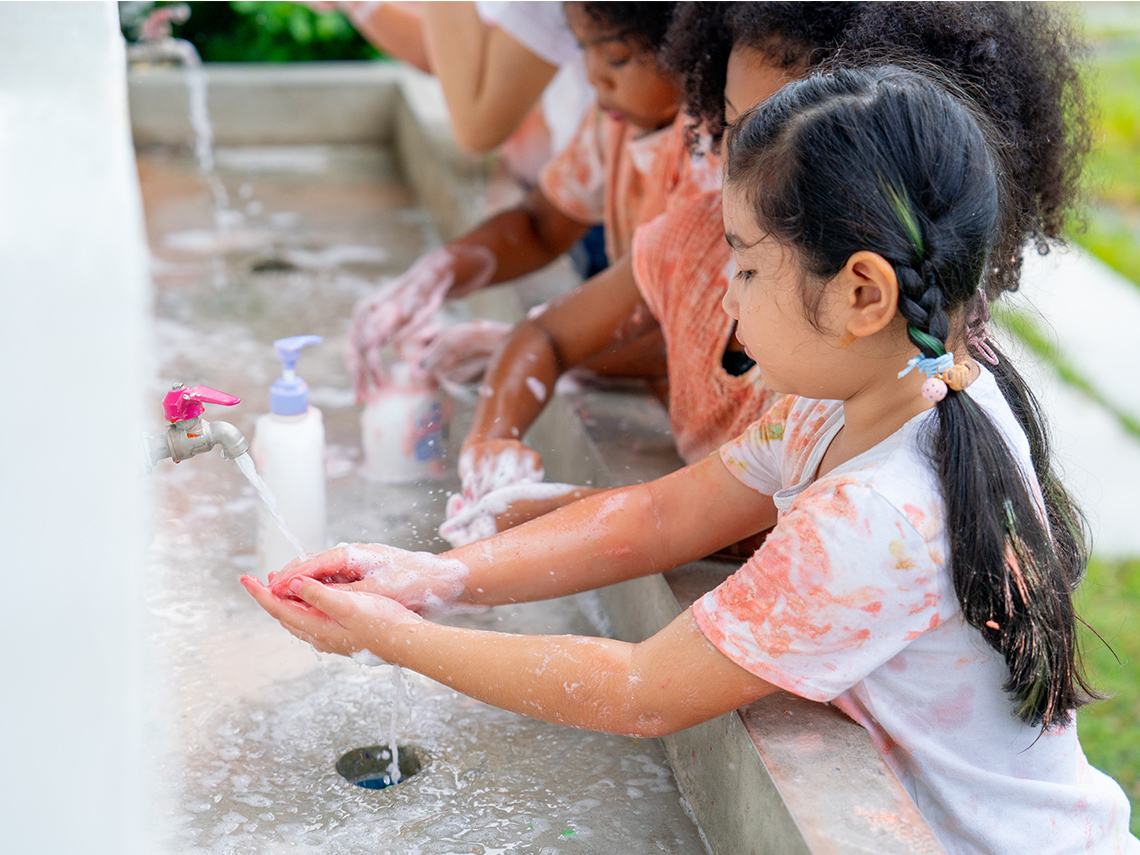 A group of children wash their hands at a sink.