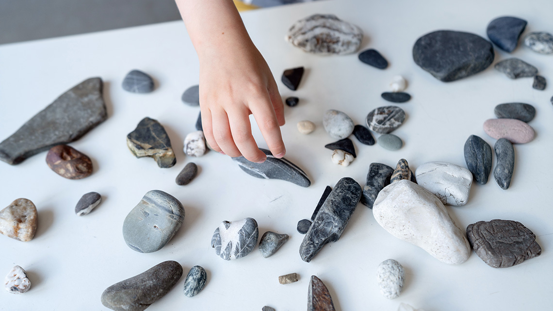 A child's hand is sorting assorted stones on a table.
