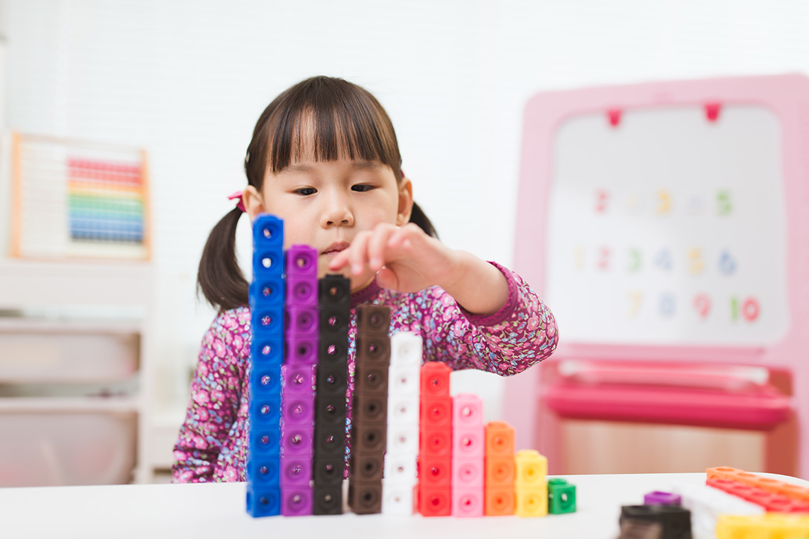 A child stacks colourful connecting cubes into tall towers on a table.