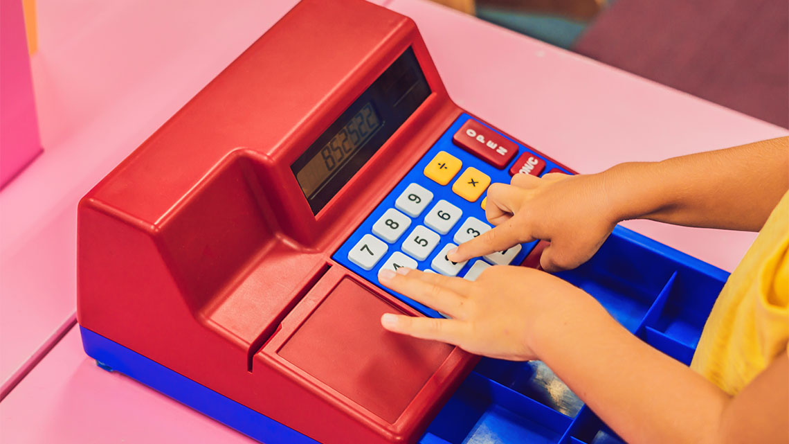 A child presses number buttons on a toy cash register