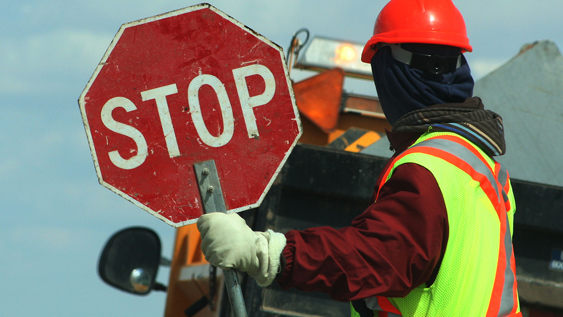 Side view of a person holding a stop sign against a vehicle on the road.