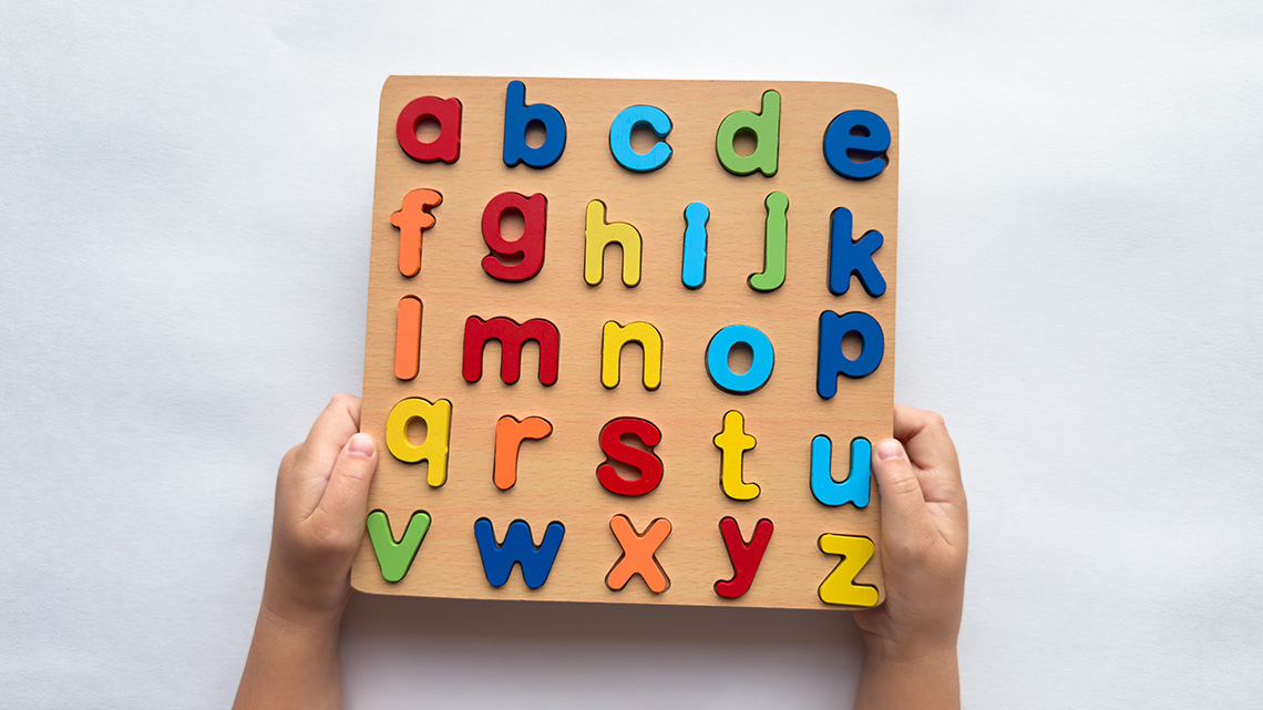 Hands holding a wooden puzzle with colourful lowercase letters from a to z.