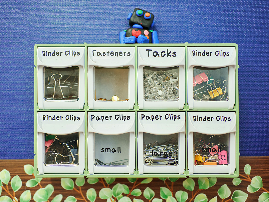 A small organizer with drawers labeled binder clips, fasteners, tacks, and paper clips.