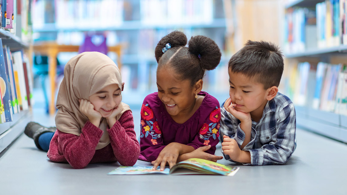 Three young children sit on the ground while reading a