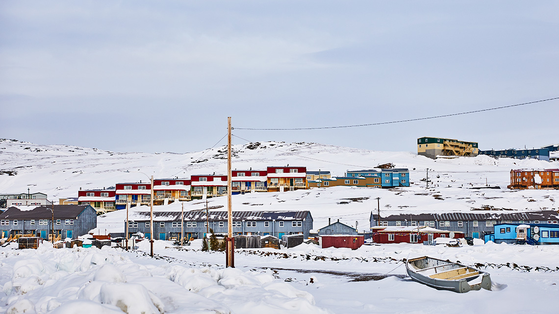 A snowy community with rows of small, colourful houses on a hillside.