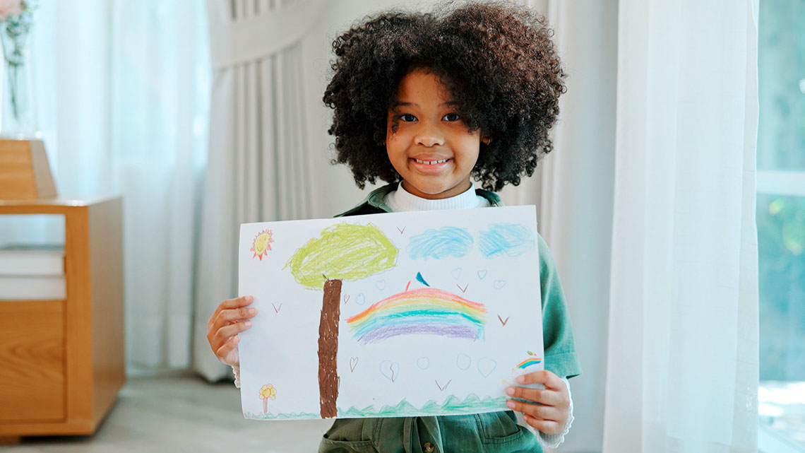 A young child holds a drawing on white paper.