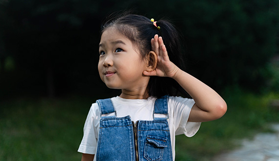 A young child raises a hand next to their ear.