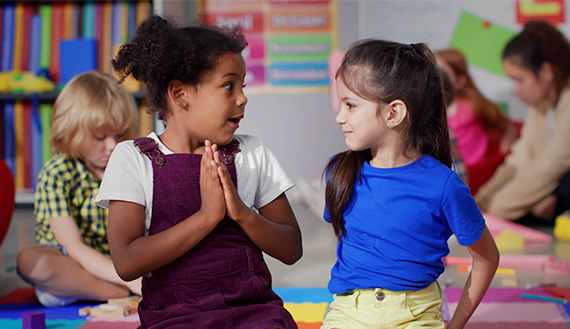 Two young children sit on the floor facing each other.