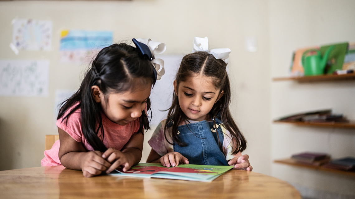 Two young children are reading a book together at a table.