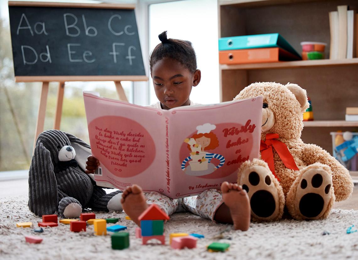 A young child reads a book while sitting on the floor.