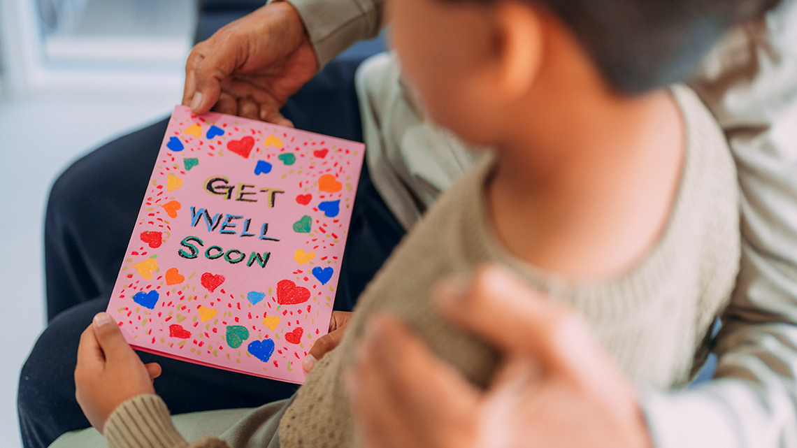A learner holds a greeting card with the text, get well soon.