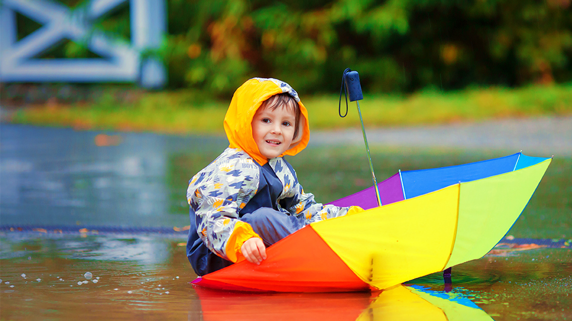 A child sitting in an upside-down umbrella on the wet ground.