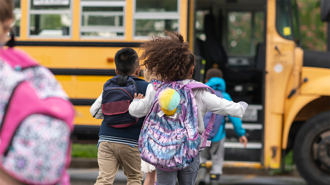 A group of kids are wearing backpacks and running to the school bus.