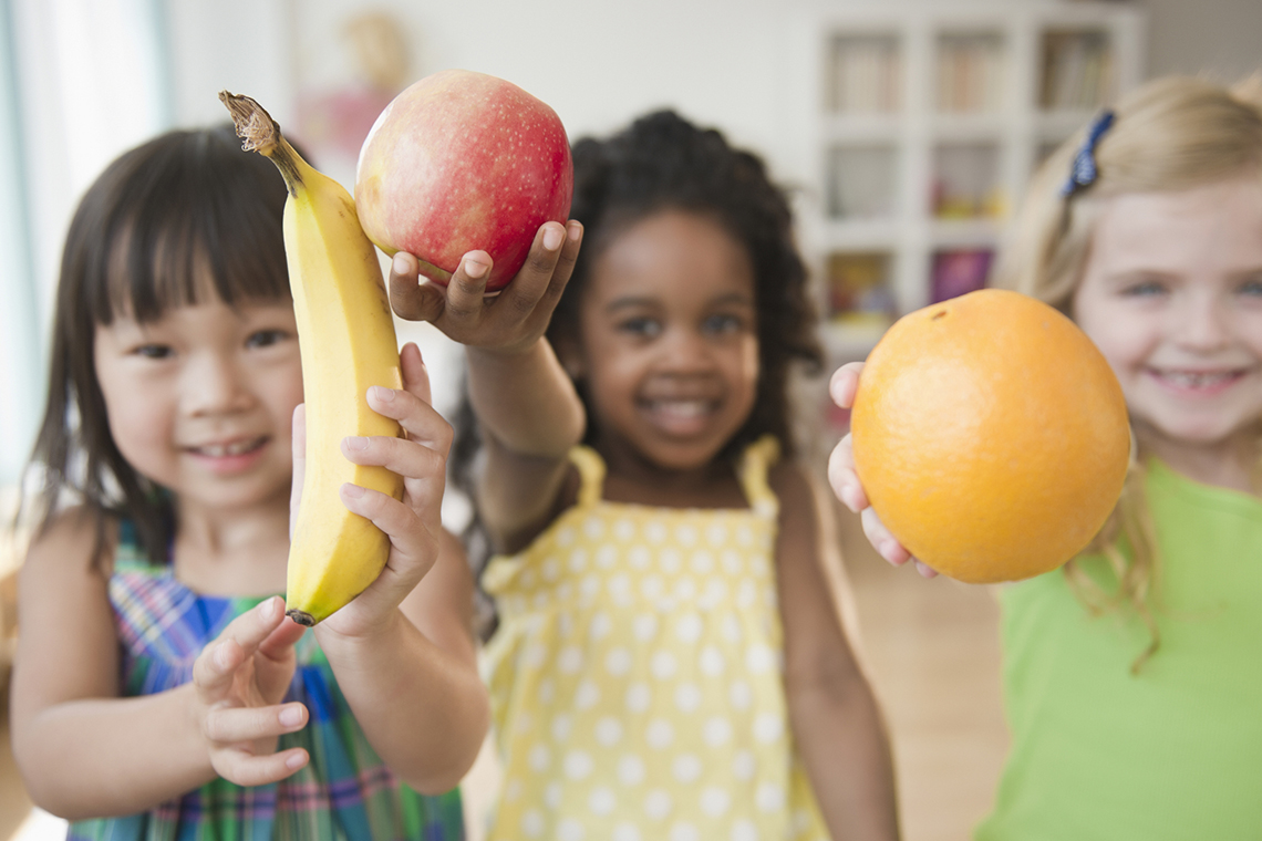 Children holding their favourite fruit: a banana, an apple and an orange.