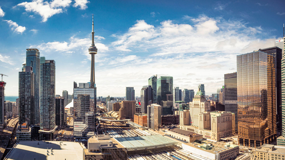 Many tall buildings made of concrete, bricks, and glass next to streets and train tracks.