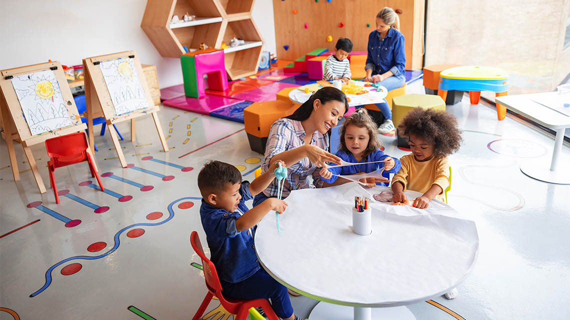 A teacher in a classroom with learners. They are sitting at a table doing an activity.