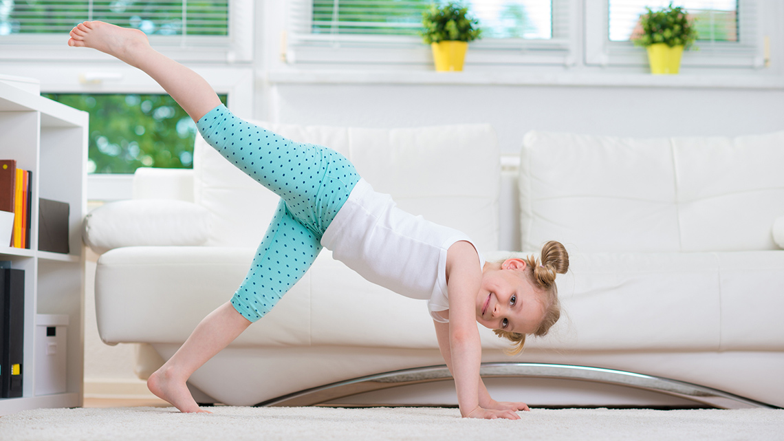 A child stretches with both hands touching the floor in front of them, with one leg raised in the air behind them.