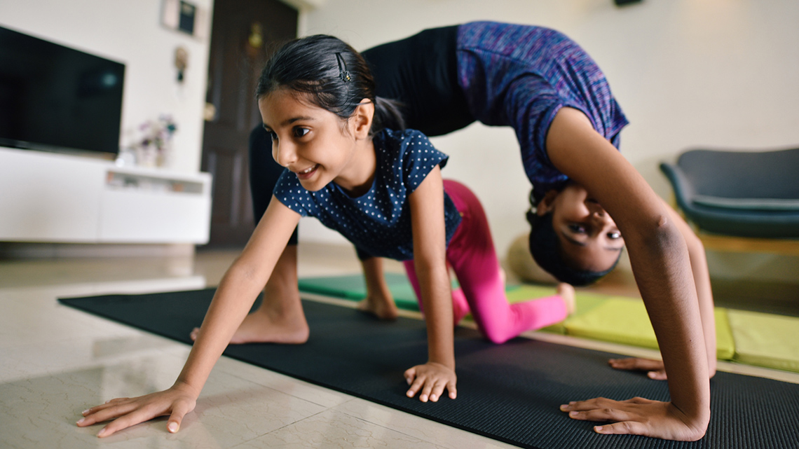 A child and an adult do stretches on yoga mats.