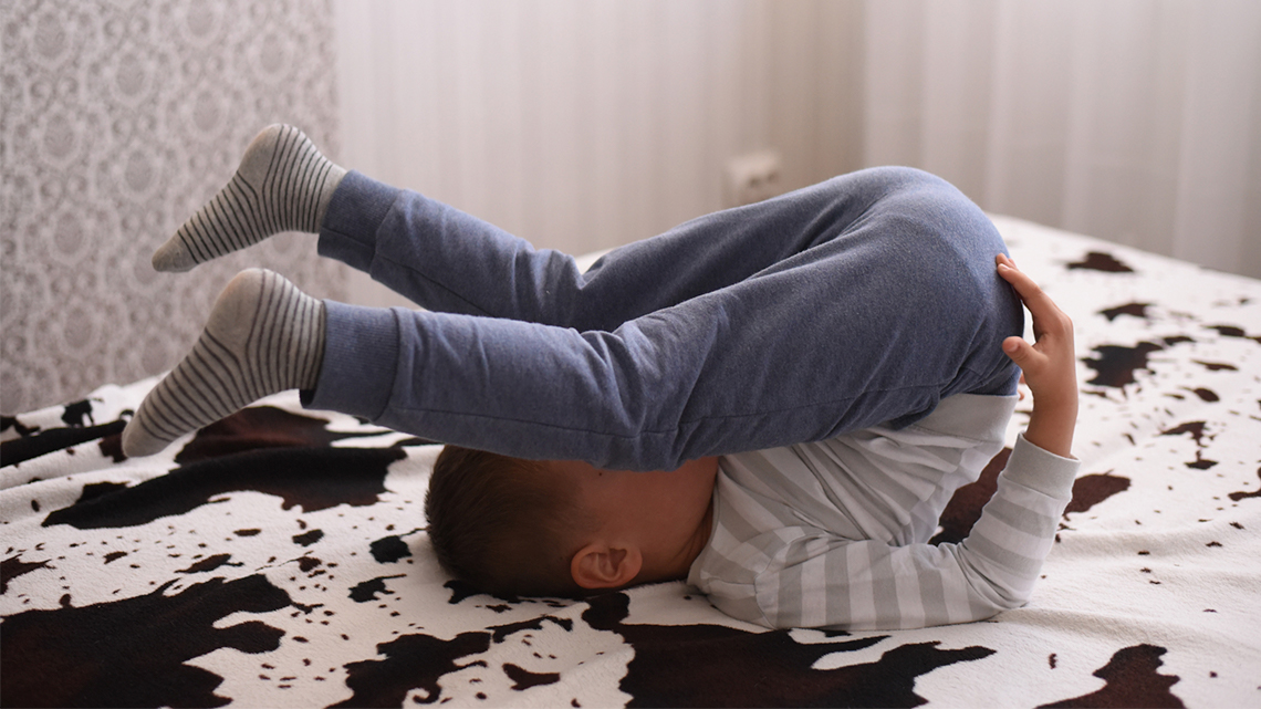 A child lies down and stretches with both legs over their head.