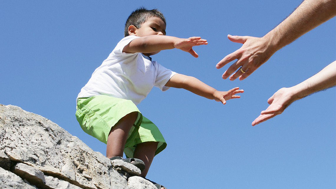 A kid who is high up and needs help getting down. They are reaching out with their arms for help.