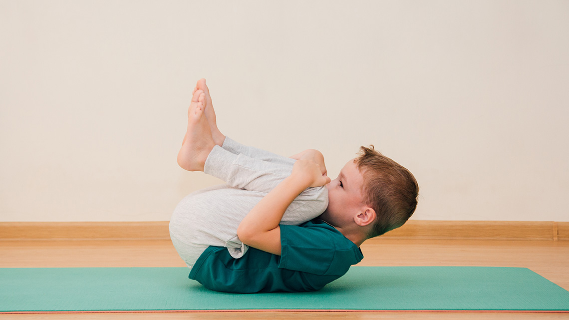 A child curls up on their back by holding their knees up to their chest.