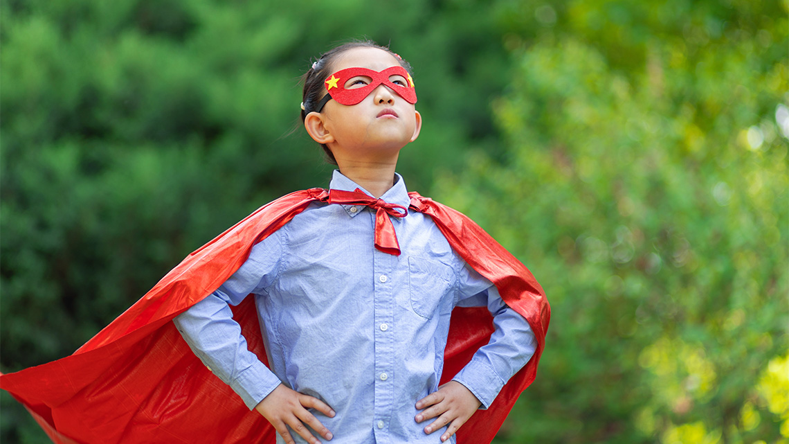 A child is standing and smiling with their hands on their hips, looking up at the sky.