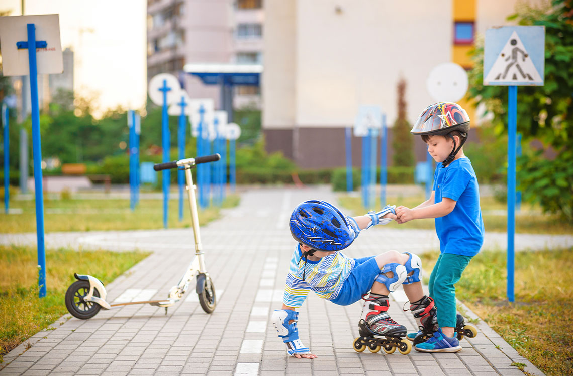 A child helps their friend up on their roller skates.
