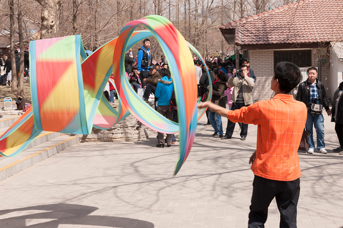 People are watching a dancer who is making colourful ribbons dance in the air.