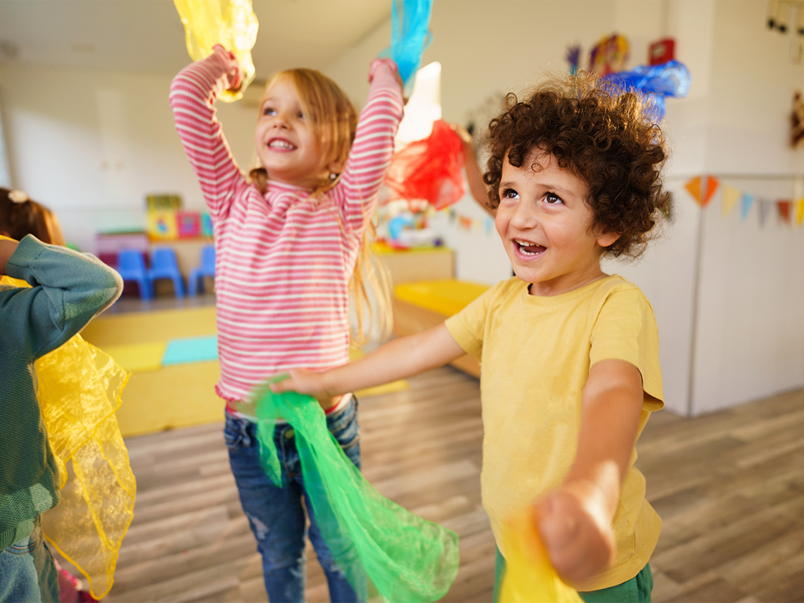 Children are smiling and dancing with scarves.