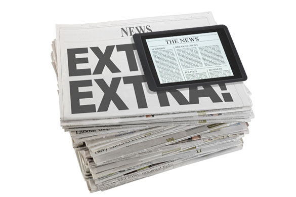 A stack of newspapers with a tablet on top displaying online news